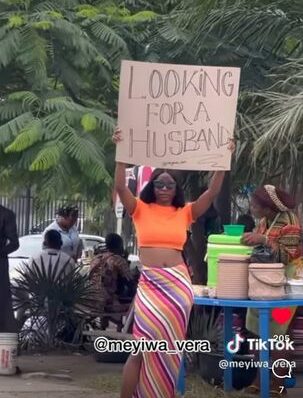 Lady carries placard on road with inscription “Looking for a husband”, men rush to take her contact